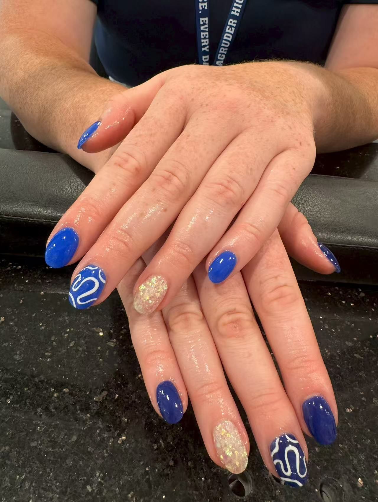Hands with blue and gold gel nails; one nail with white design, others solid.