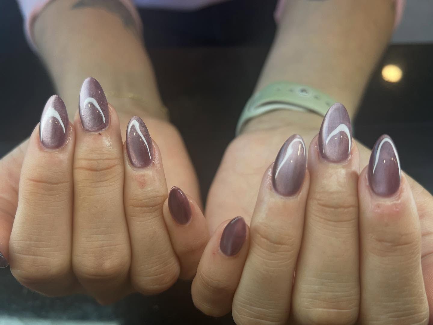 Hands with oval-shaped nails painted mauve with white cat-eye stripe.