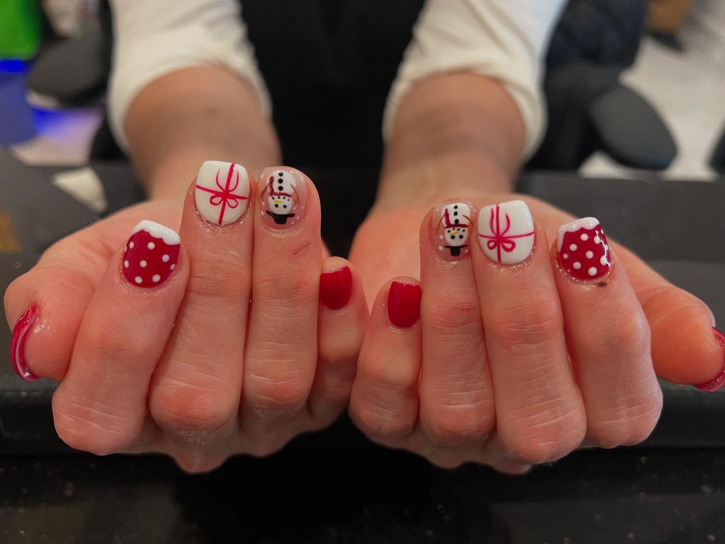 Woman's hands with Christmas-themed nail art. Red and white designs: polka dots, snowmen, and gifts.