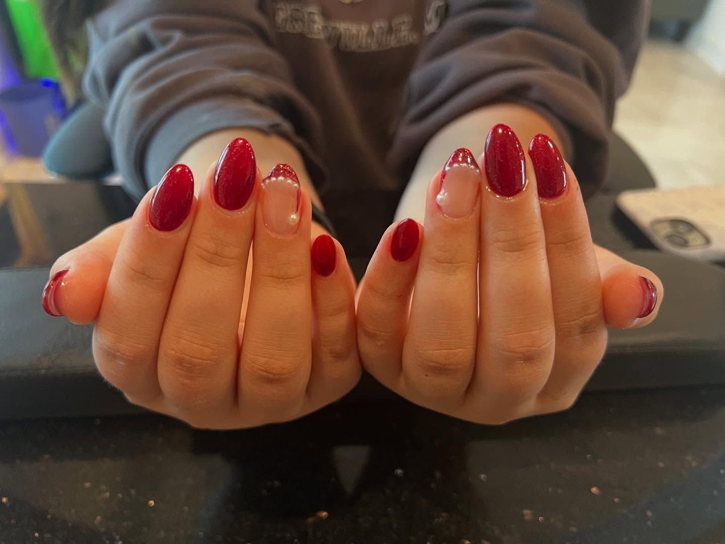Hands with red and nude almond-shaped nail polish, in front of a neutral background.