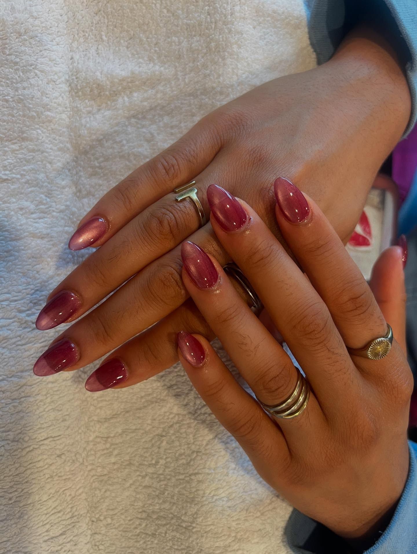 Hands with long, polished nails in shades of pink, wearing rings on several fingers.