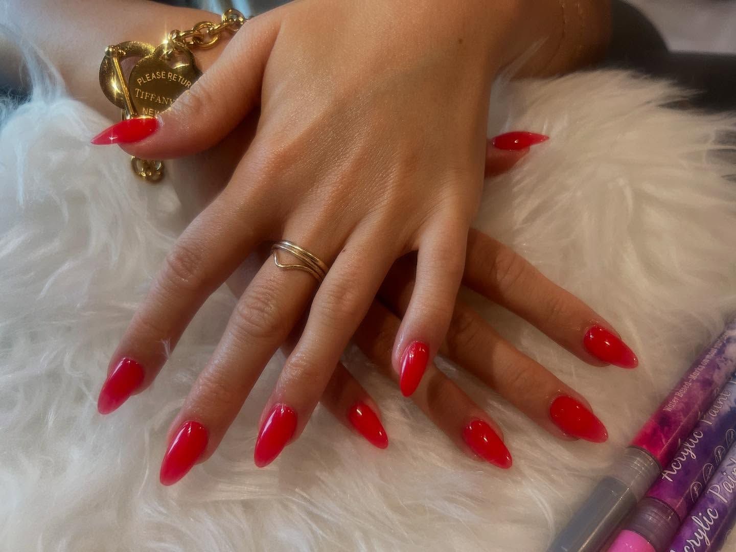 Hands with long, red, glossy acrylic nails and a gold ring.