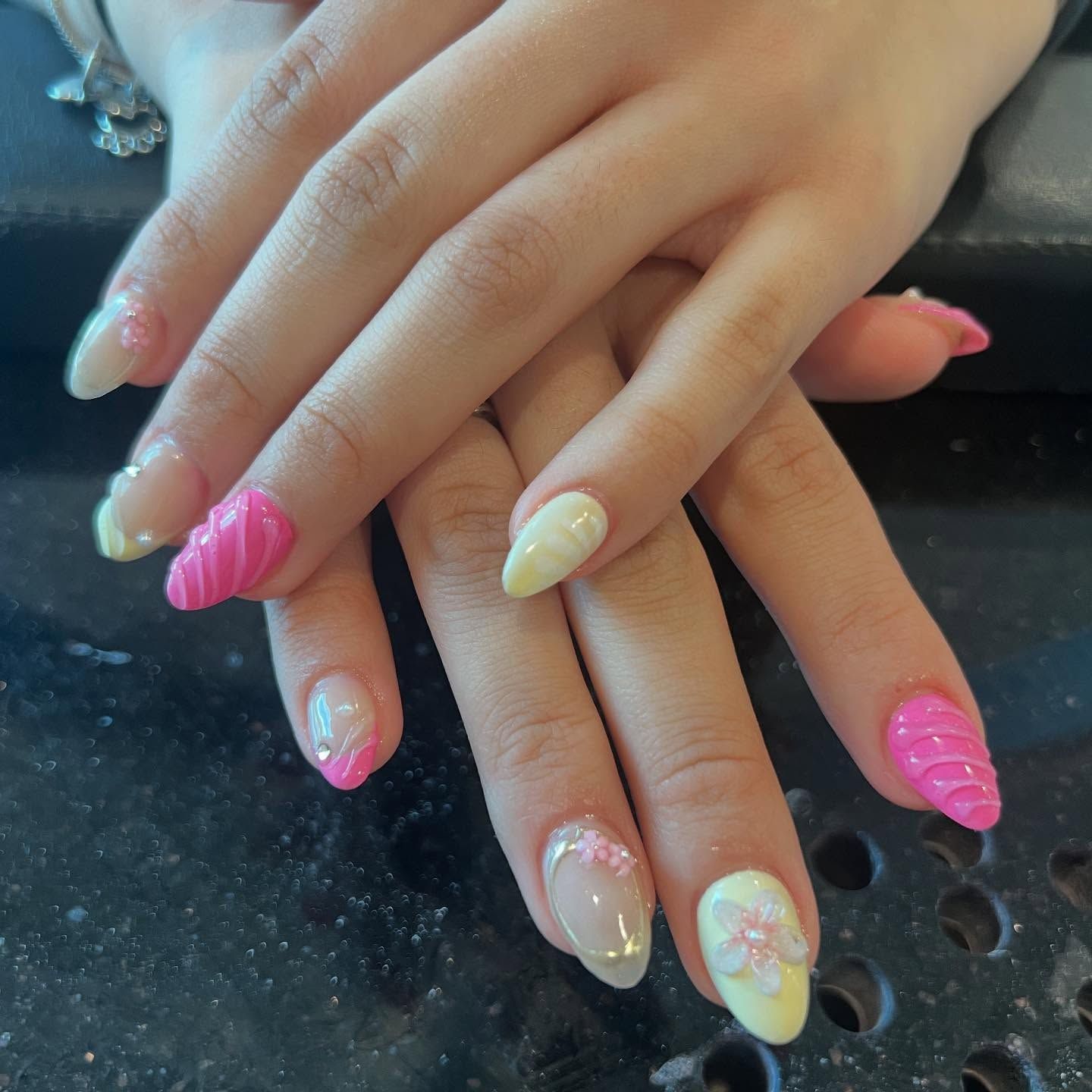 Hands with almond-shaped nails, some pink and yellow with floral and swirl designs.