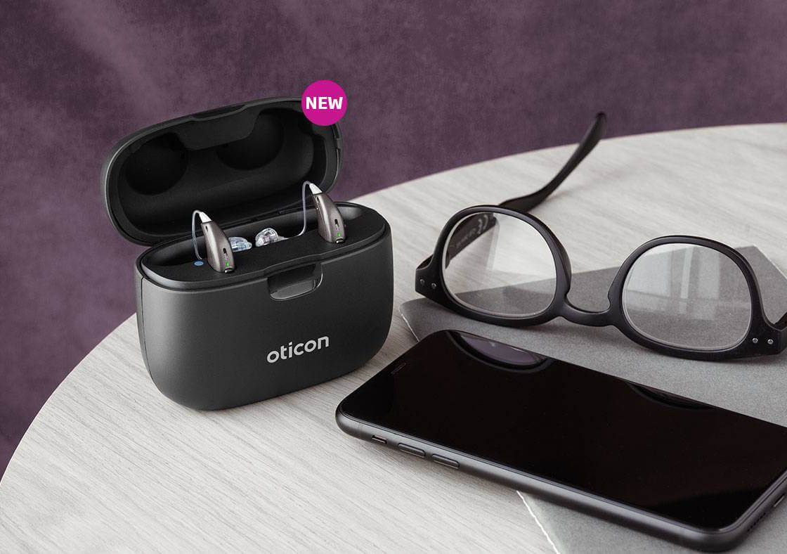 A pair of hearing aids is sitting on a table next to a cell phone and glasses.