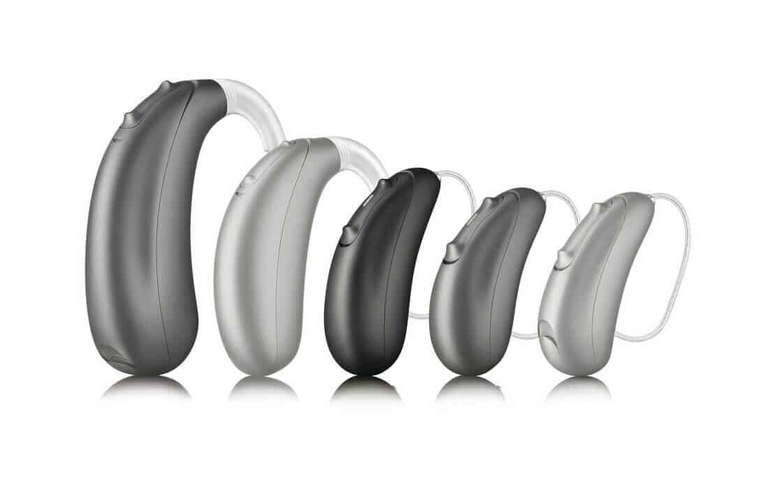 A group of hearing aids are lined up in a row on a white surface.