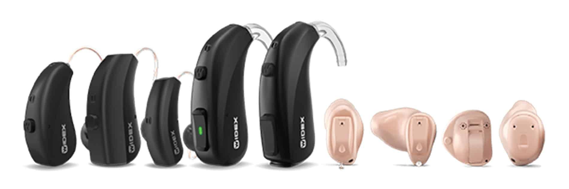 A variety of hearing aids are lined up in a row on a white background.