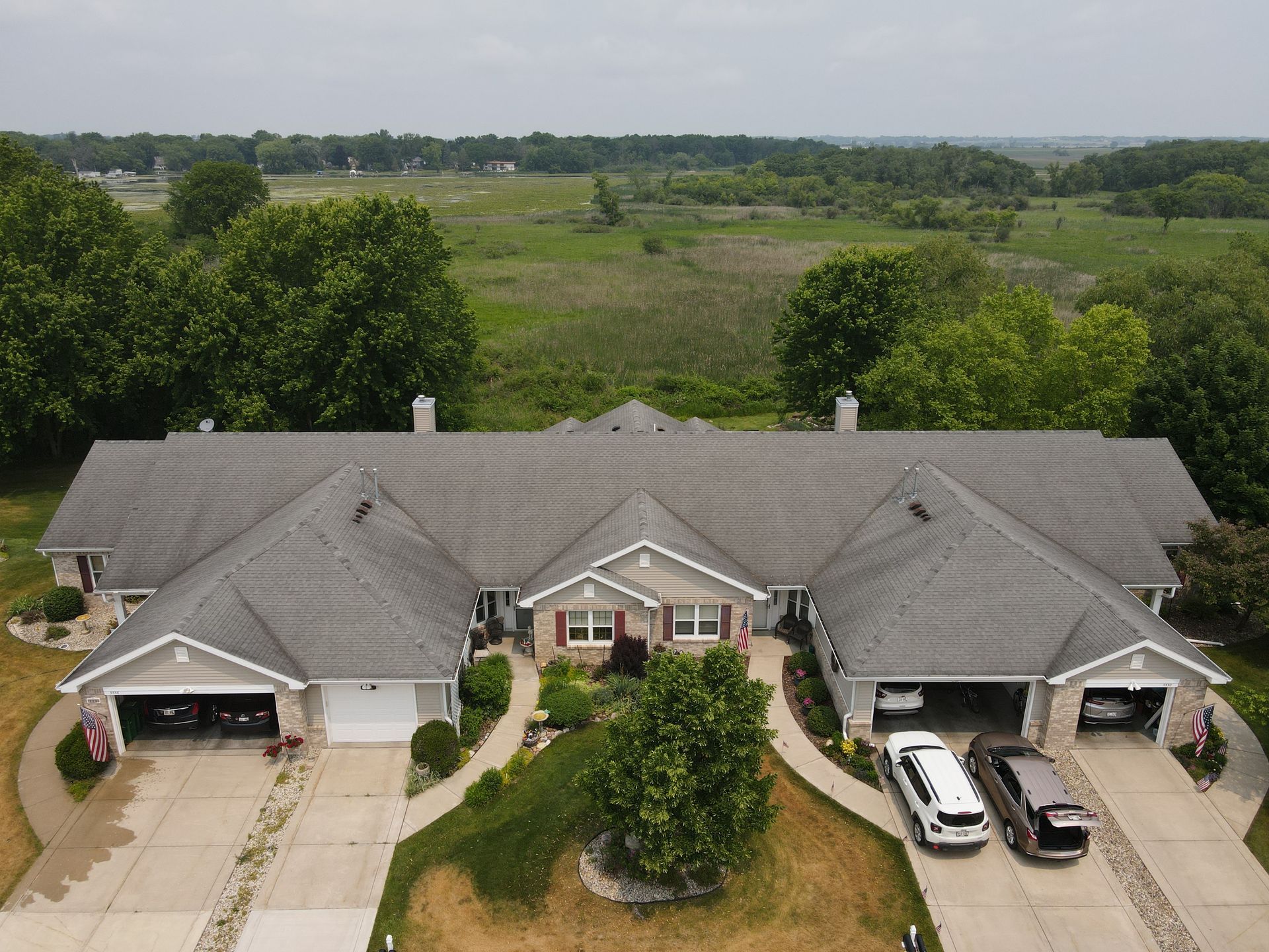 Overhead view of a multi-unit residential building with garages, surrounded by trees and a field.