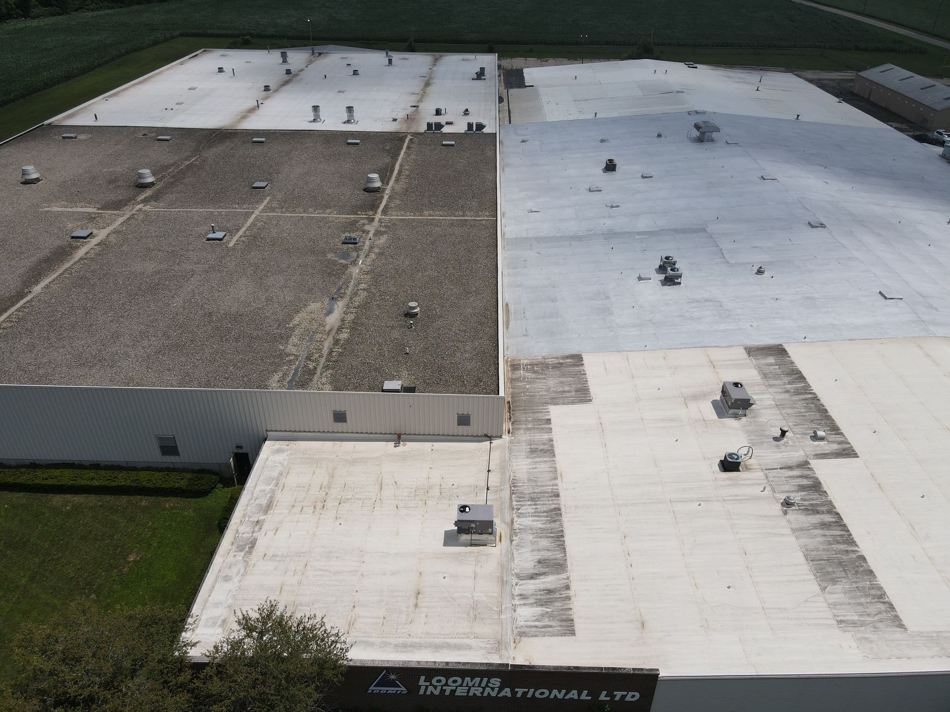 Aerial view of a commercial building with a roof partially coated in white, showing contrast between old and new.