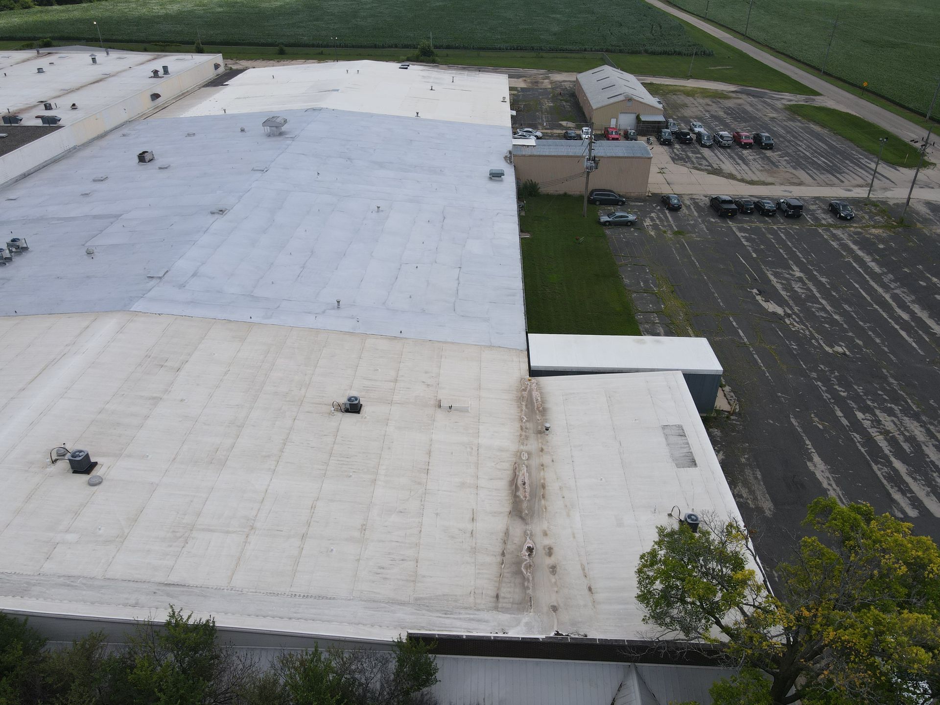 Aerial view of a large commercial building with a white roof and parking lot next to green fields.