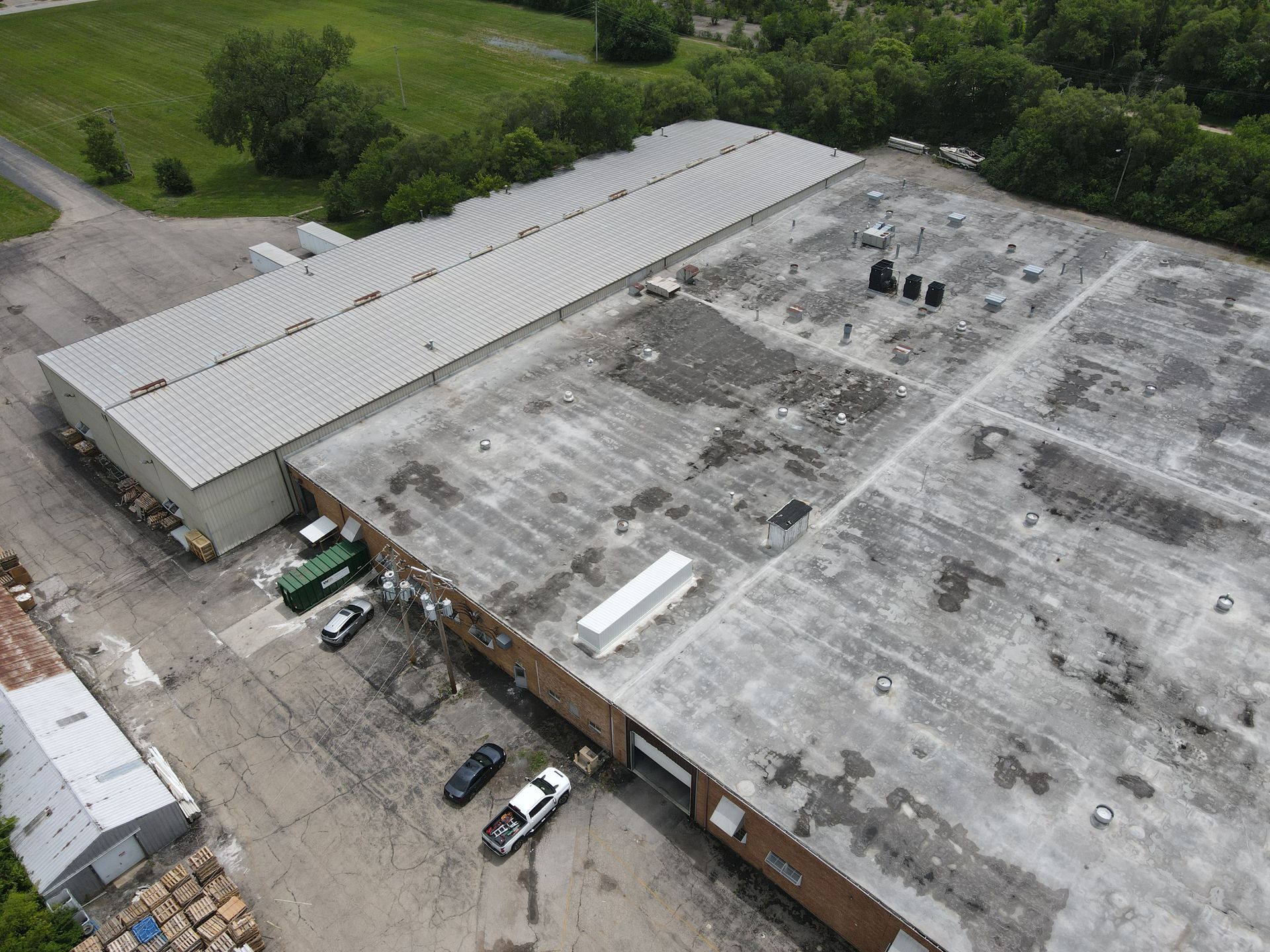 Aerial view of a large industrial building with a corrugated metal roof and various vehicles parked nearby.