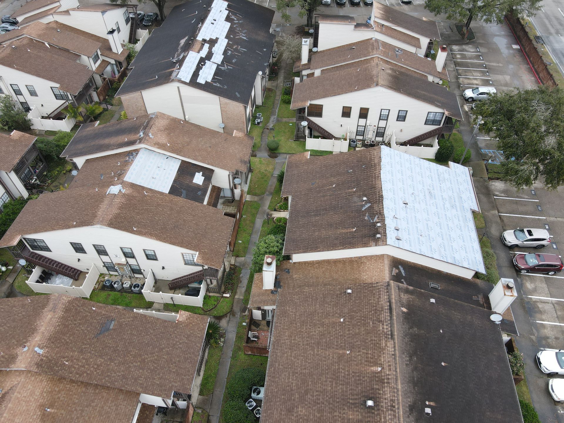 Aerial view of townhouses with brown roofs and a narrow pathway between them; parking lot on right.