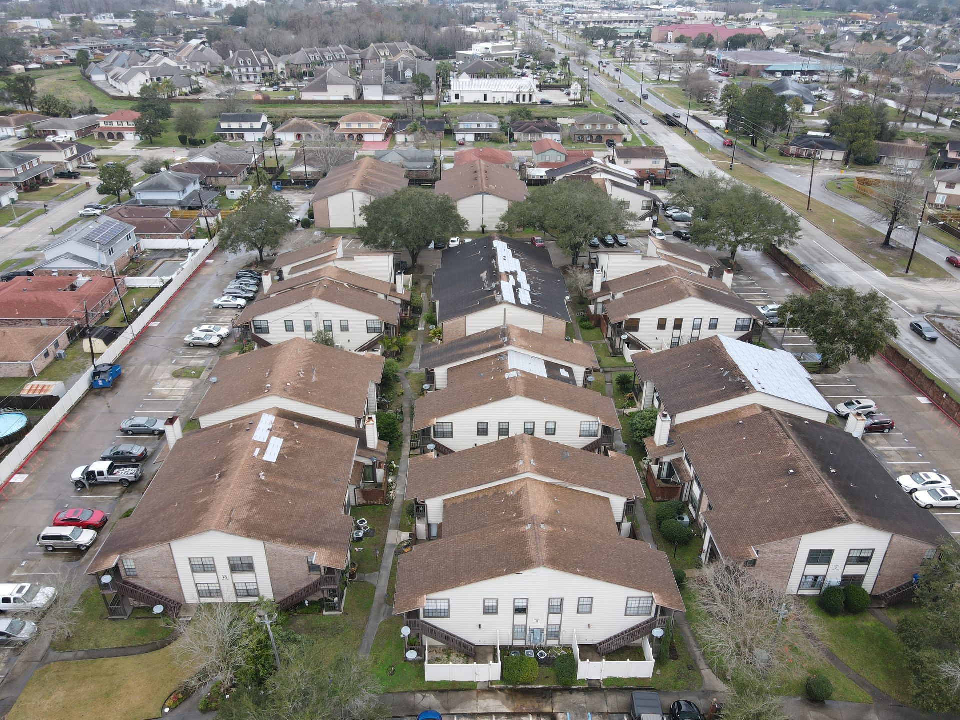 Aerial view of apartment buildings with brown roofs and parked cars along a road.