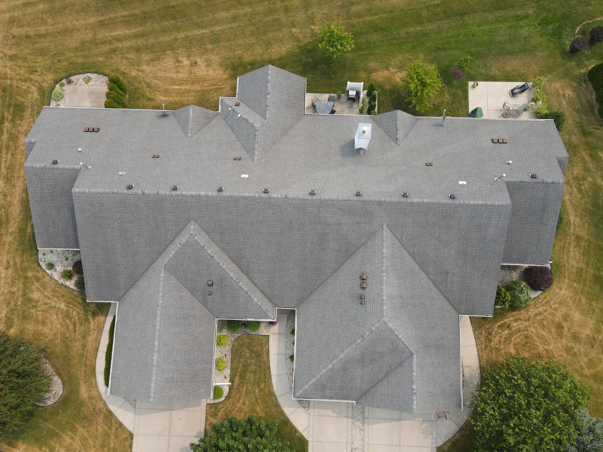 Aerial view of a gray-roofed house with landscaping and a driveway in a grassy setting.