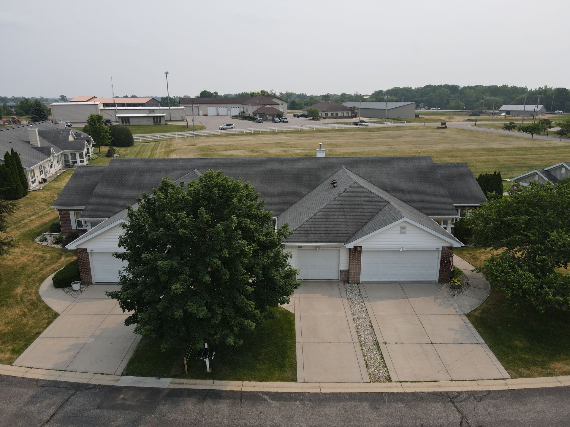 A two-unit residential building with white garage doors and a gray roof, set in a suburban landscape.