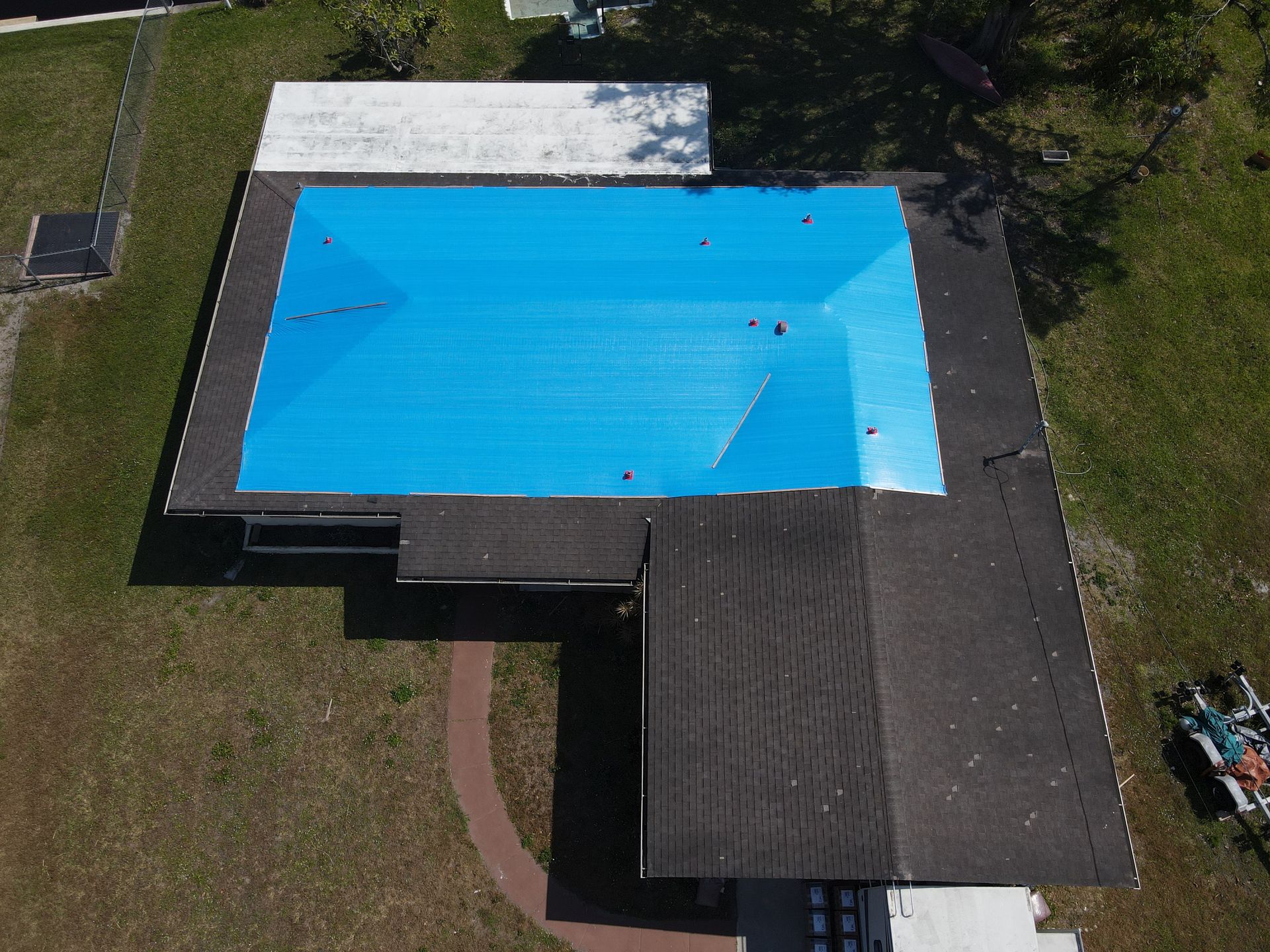 Aerial view of a house with a blue tarp covering a roof, surrounded by green grass.