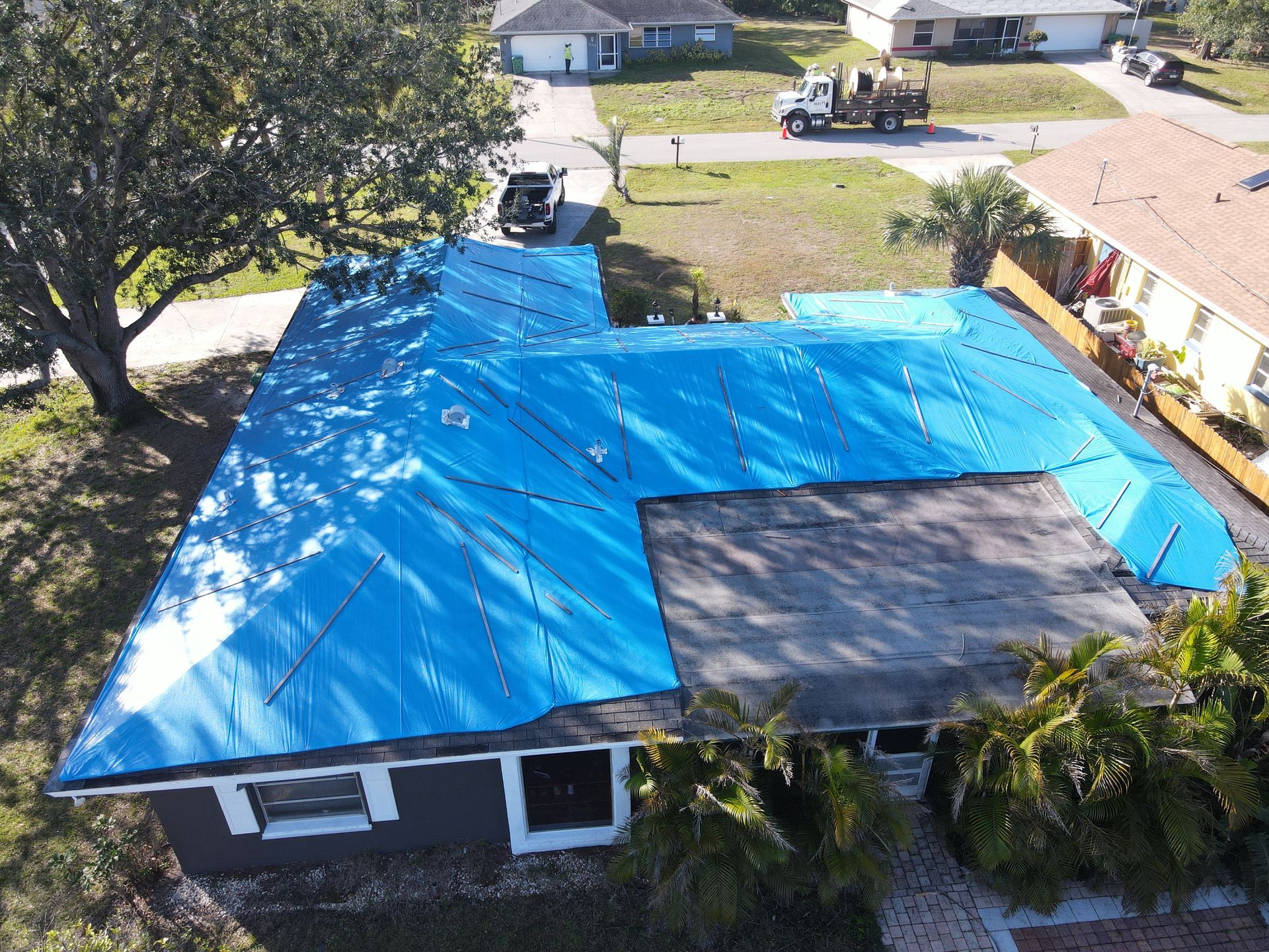 Aerial view of a house with sections of blue tarp covering the roof.