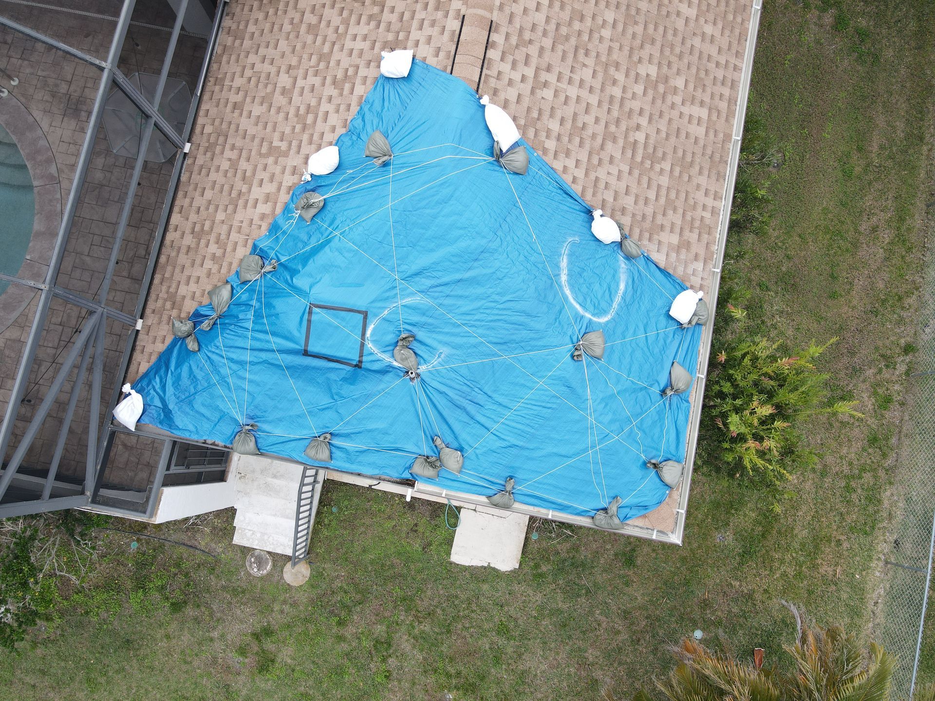Aerial view of a blue tarp covering a roof, held down by weights.