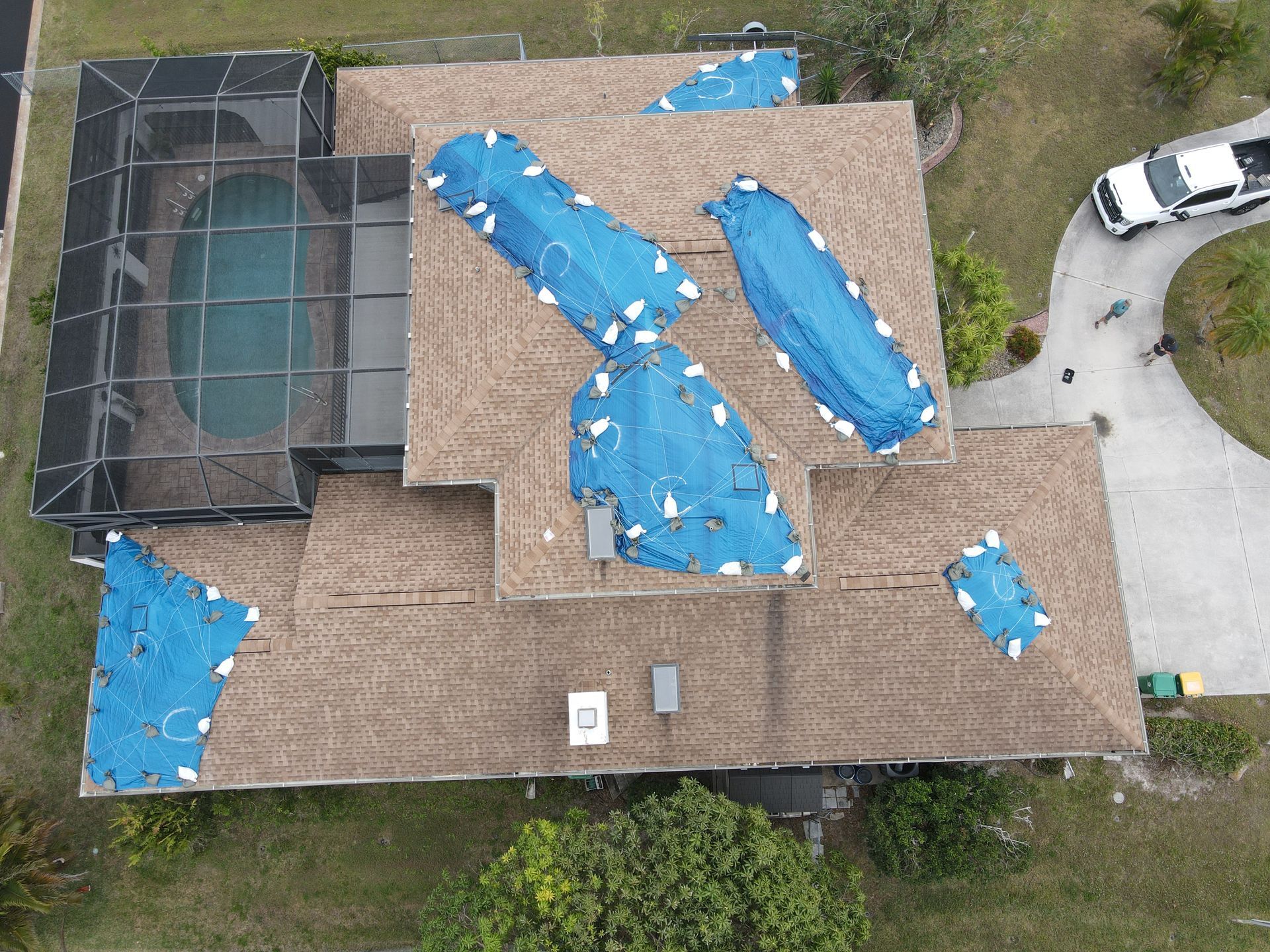 Overhead view of house with blue tarps on the roof, pool, and white truck in the driveway.
