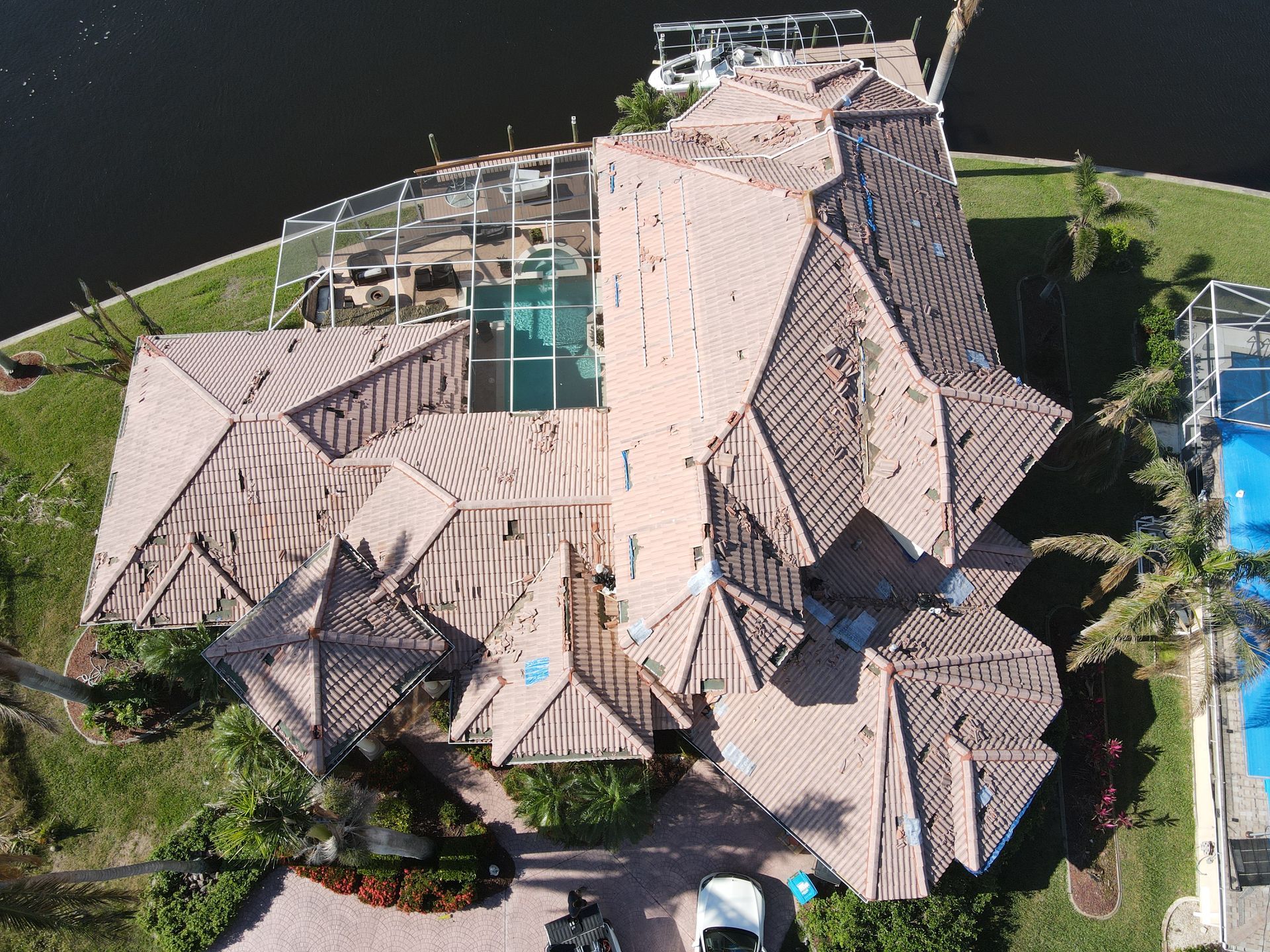 Aerial view of a large house with a tile roof, pool, and a waterfront.