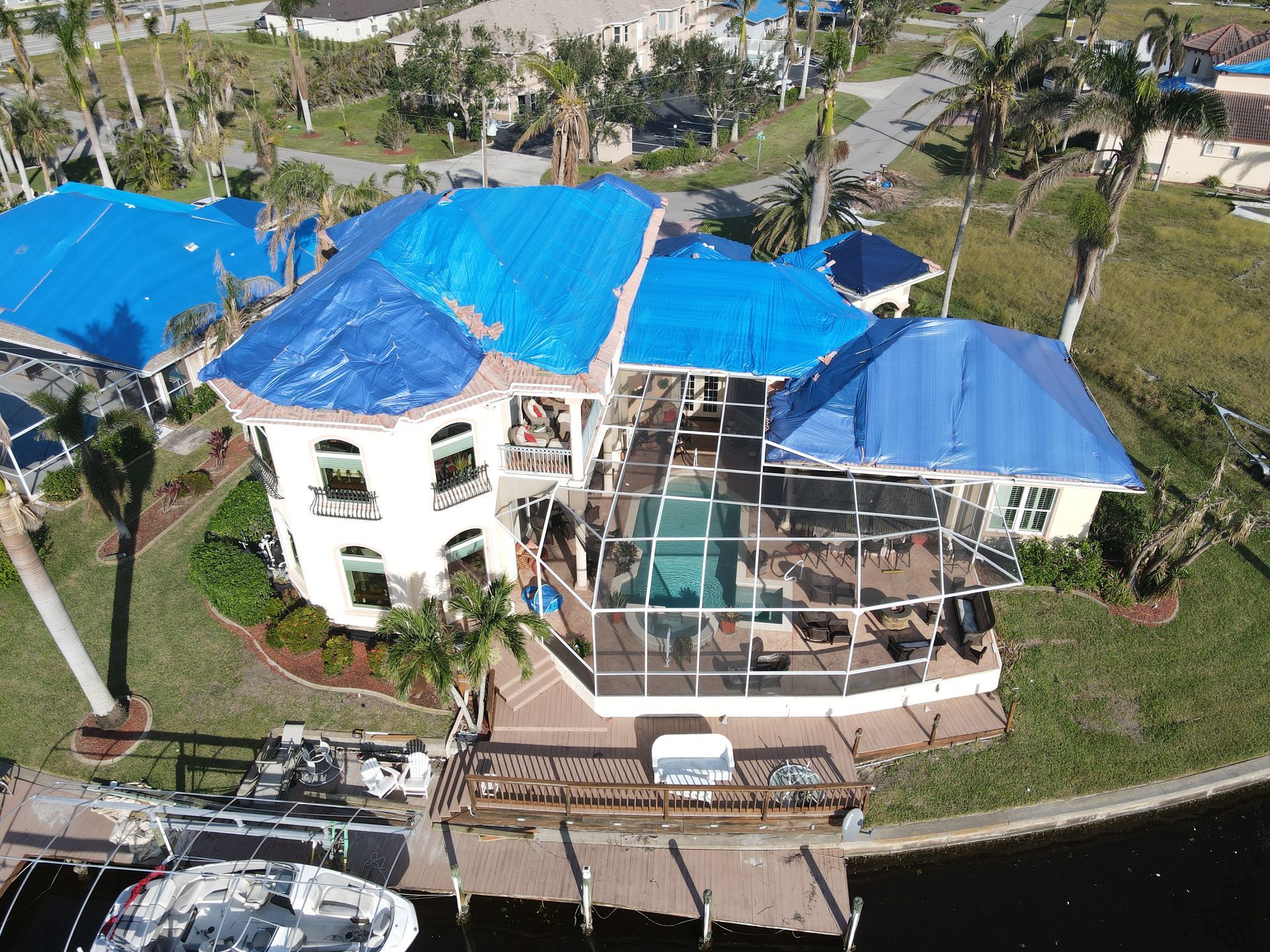 House with blue tarp on roof after a storm.  Pool and dock visible.