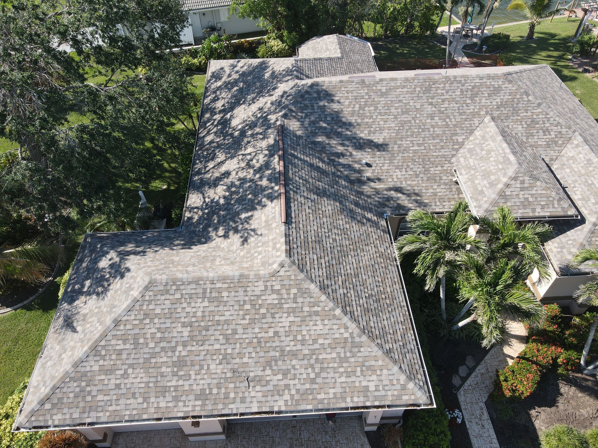 Aerial view of a gray shingle roof on a house with surrounding green trees and grass.