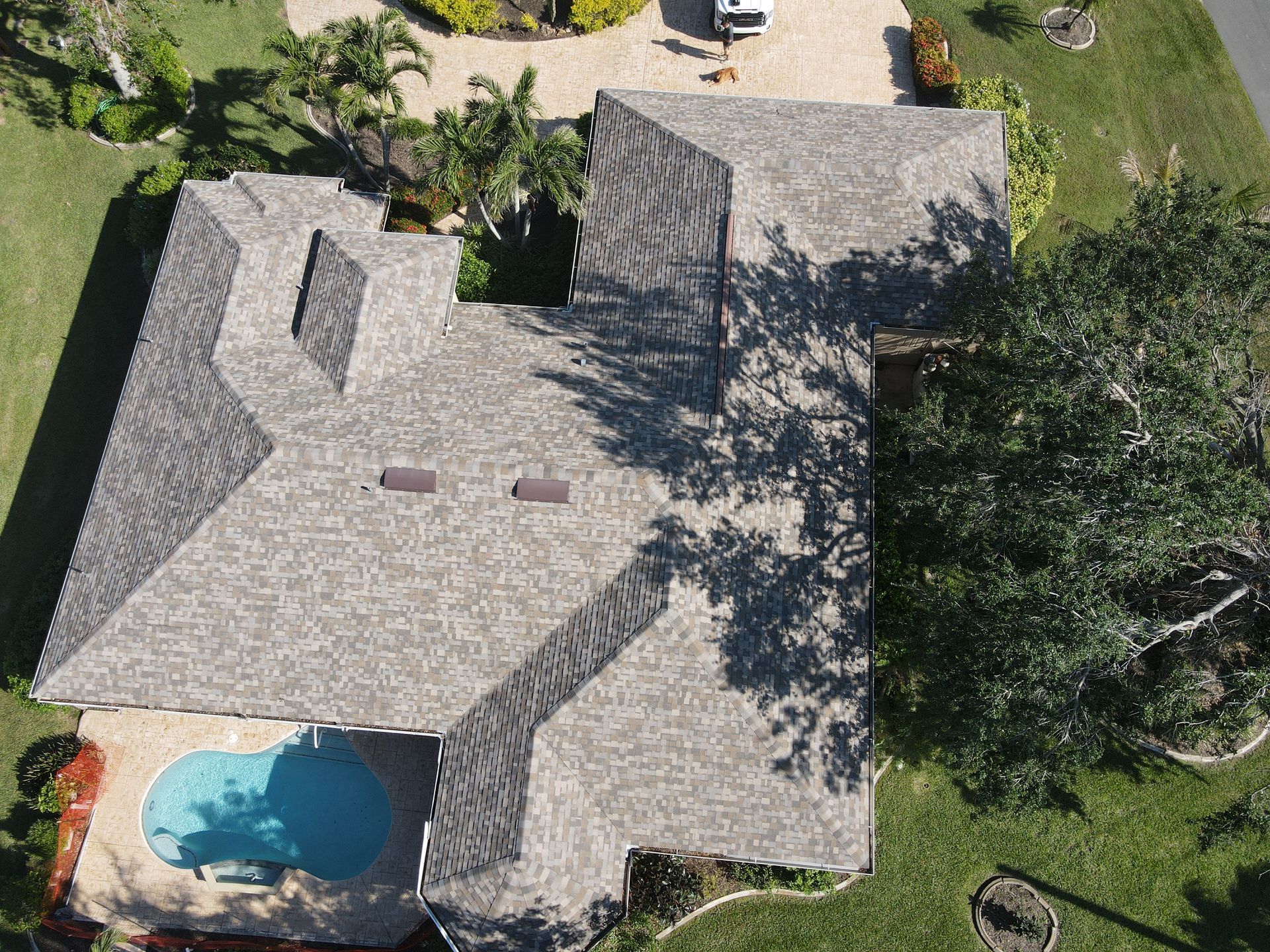 Aerial view of a house with a gray shingle roof, pool, and surrounding green lawn.
