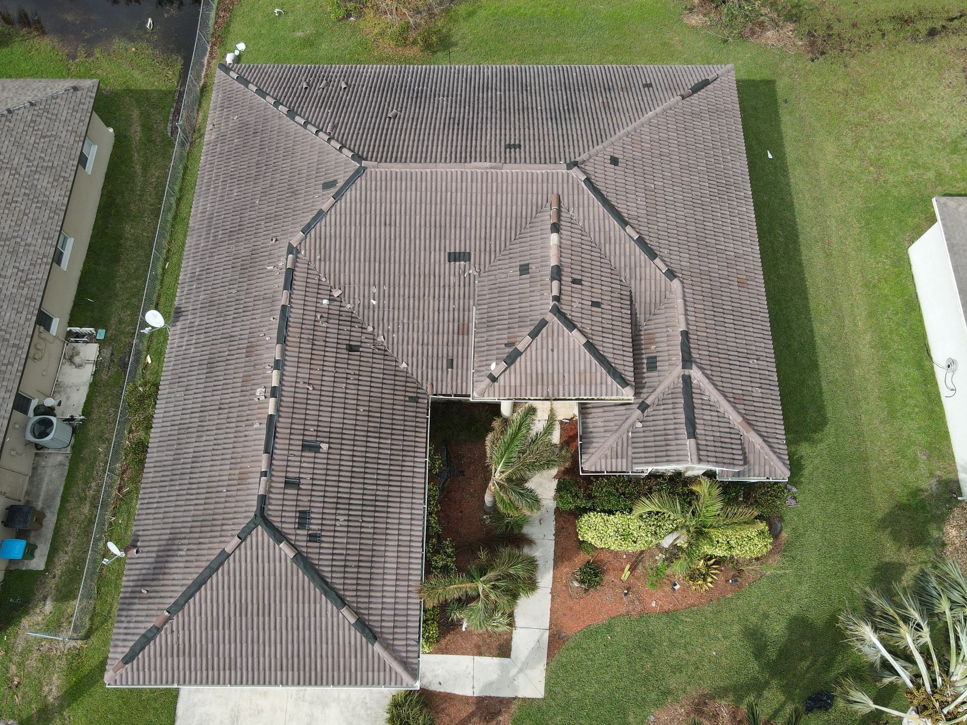 Overhead view of a house with a brown, multi-faceted roof. The house is surrounded by green grass.