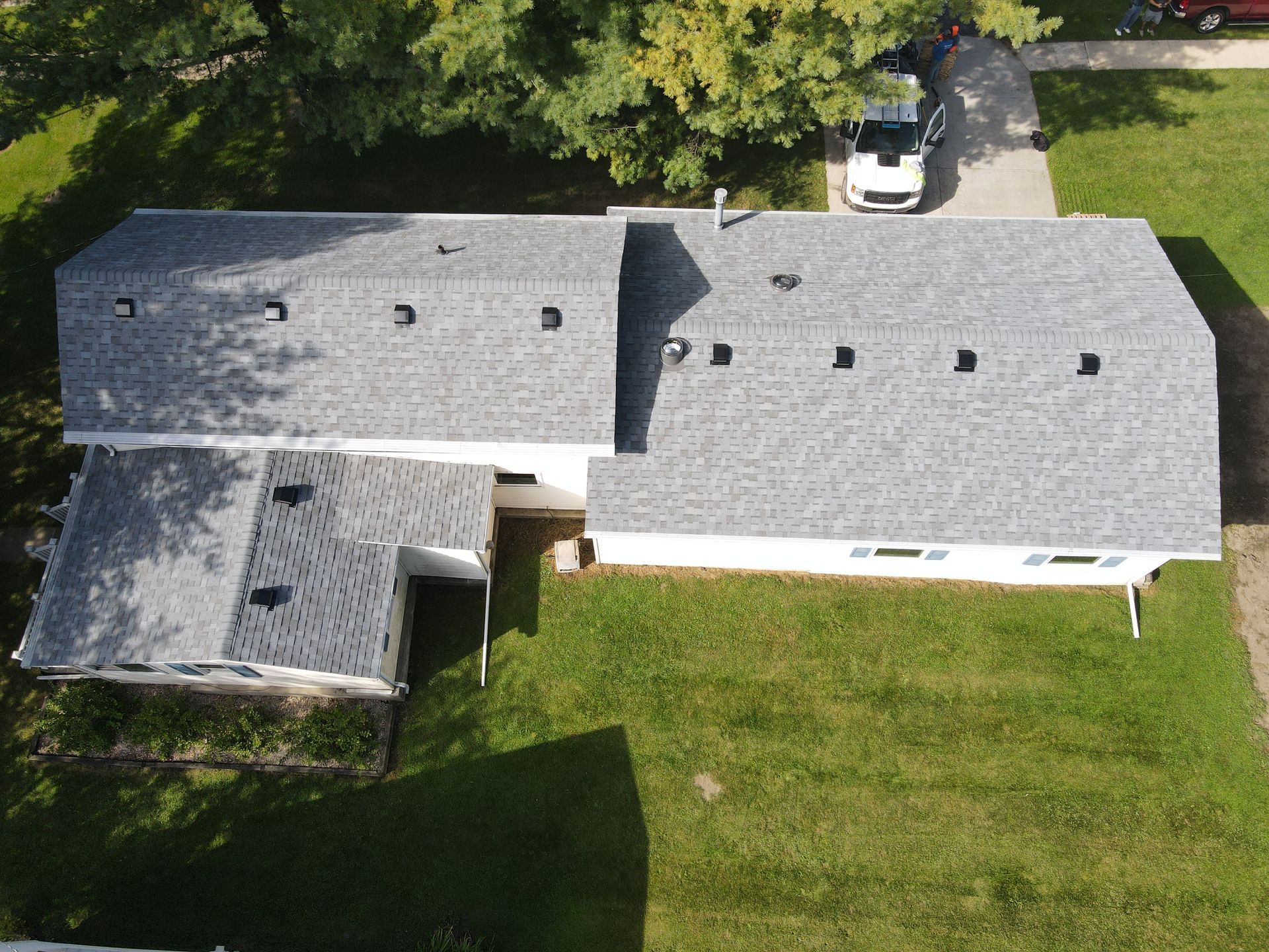 Overhead view of a house with a gray roof, a car in the driveway, and green grass.
