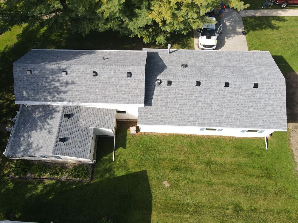 Overhead view of a house with a gray roof, surrounded by green grass. A white car is parked in the driveway.
