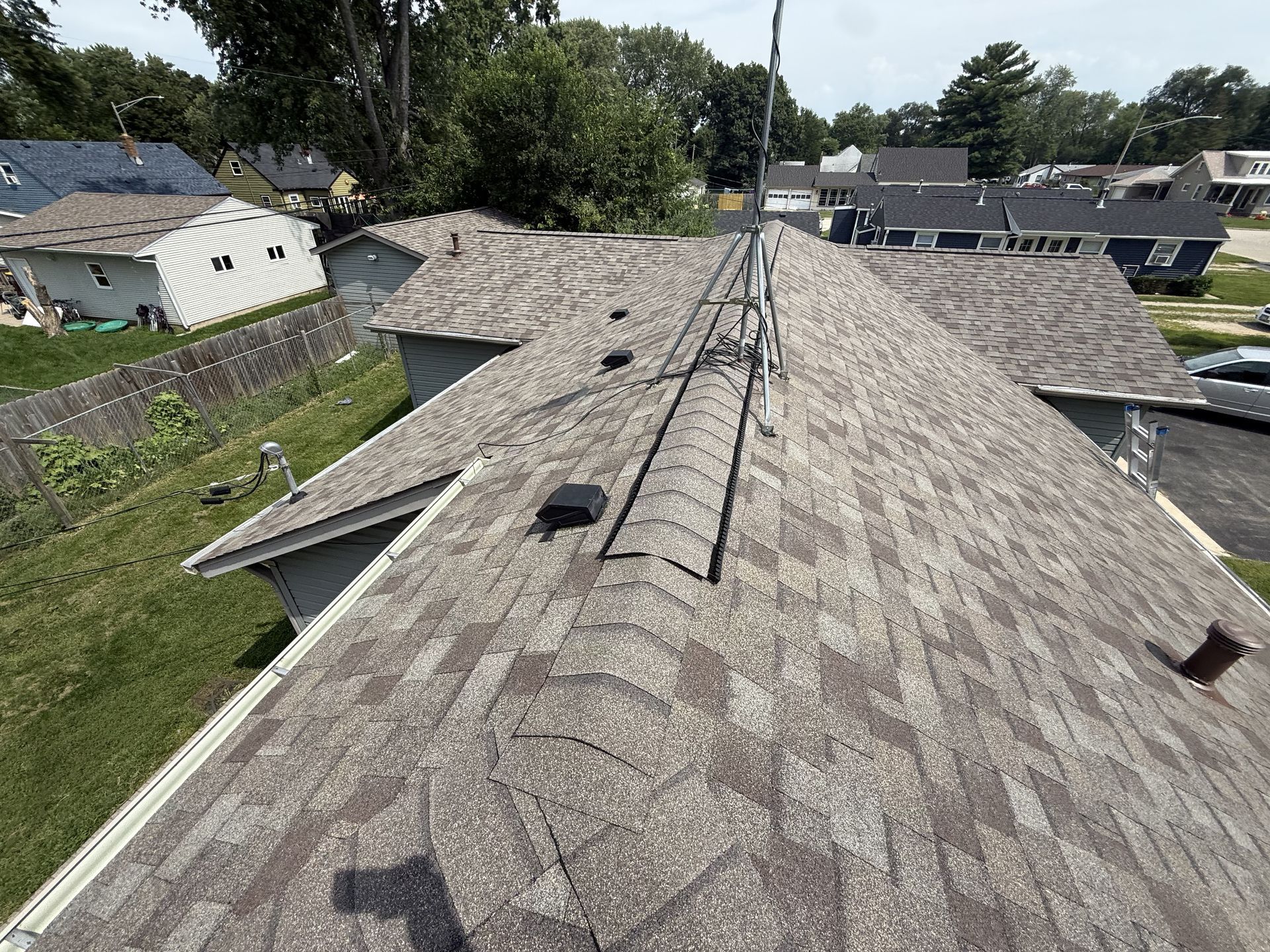 Gray asphalt shingle roof on a house, angled view. Several vents and a metal ridge vent are visible.