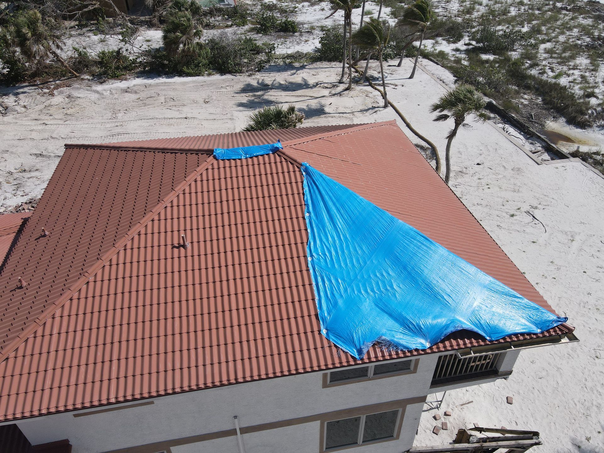 House with red tiled roof partially covered by blue tarp after damage.