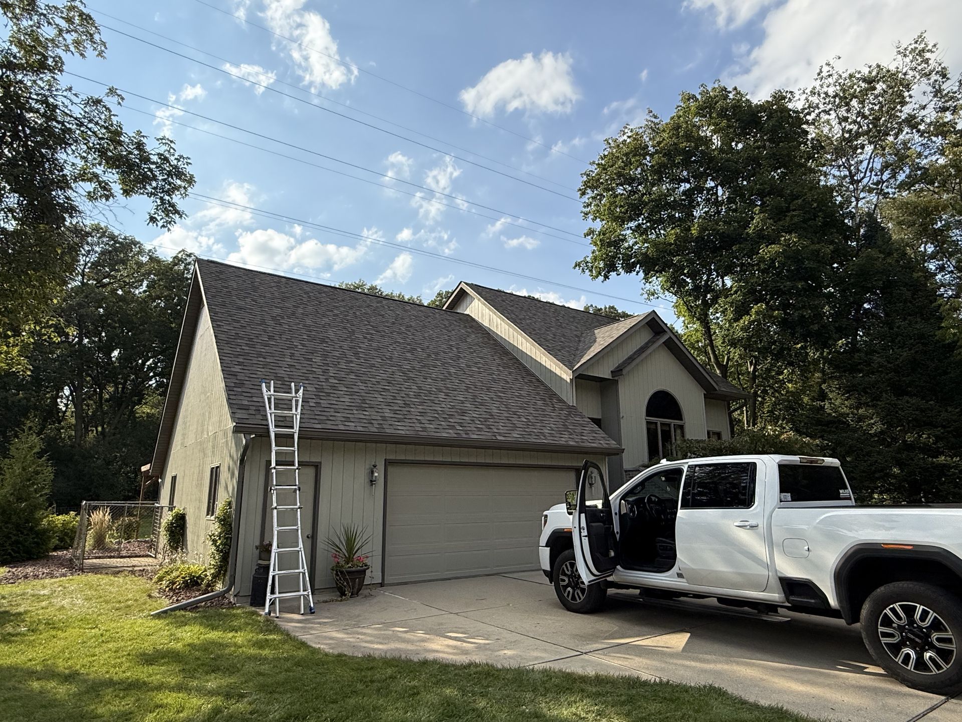 House with a gray roof and garage. A white truck is parked with its door open. A ladder leans on the side.