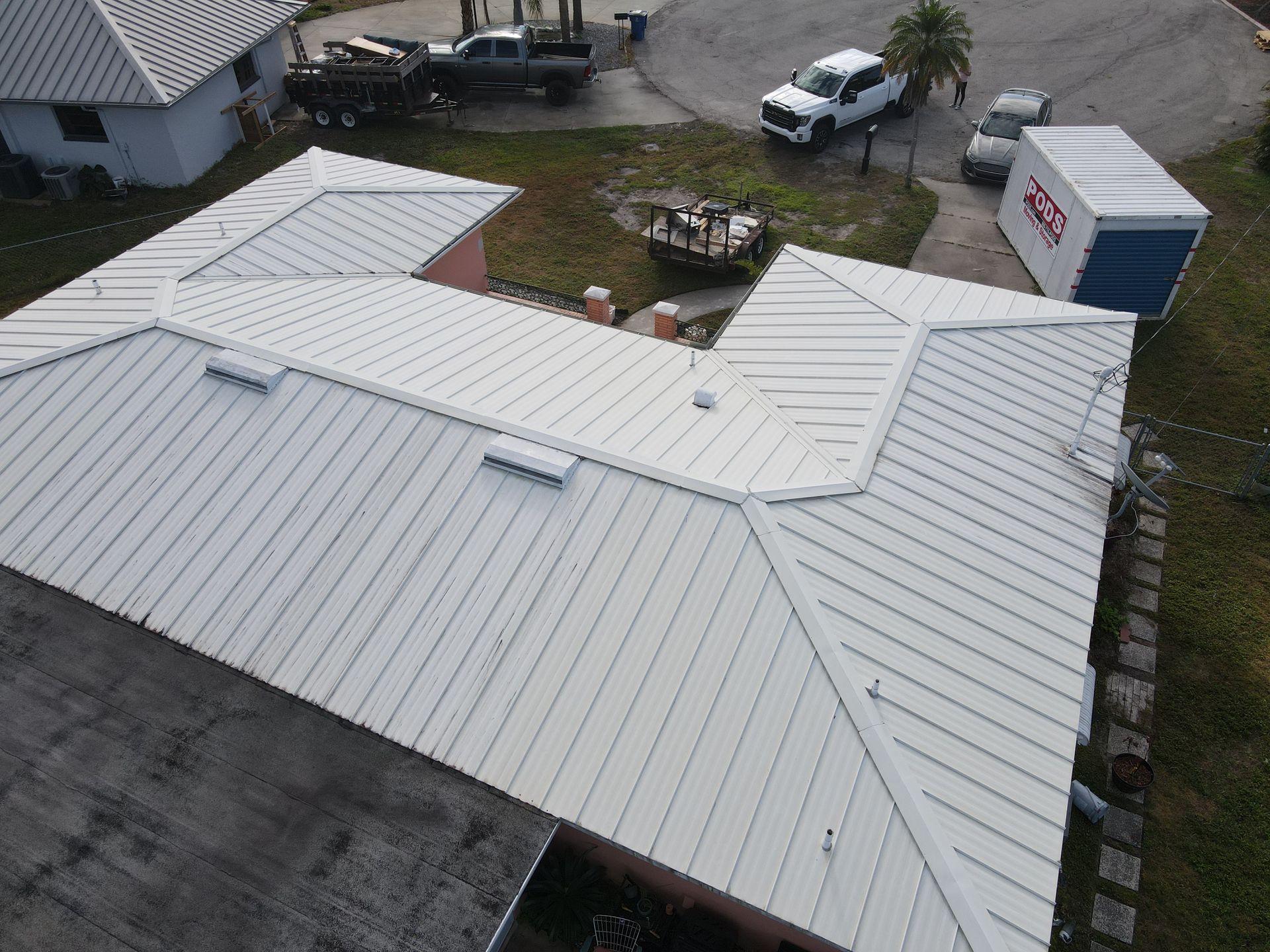 White metal roof on a house, angled view from above, vehicles and yard in the background.