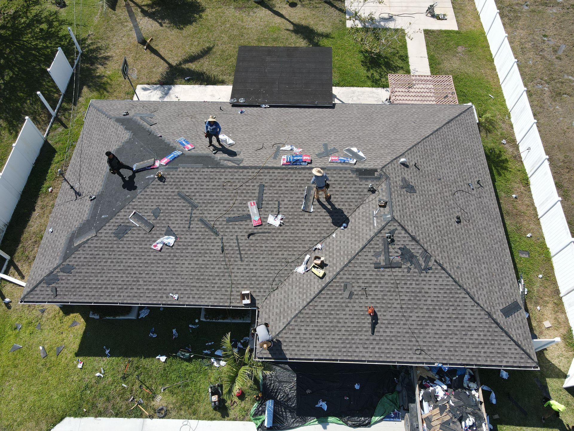 Overhead view of a dark roof with several workers inspecting damage from storm debris.