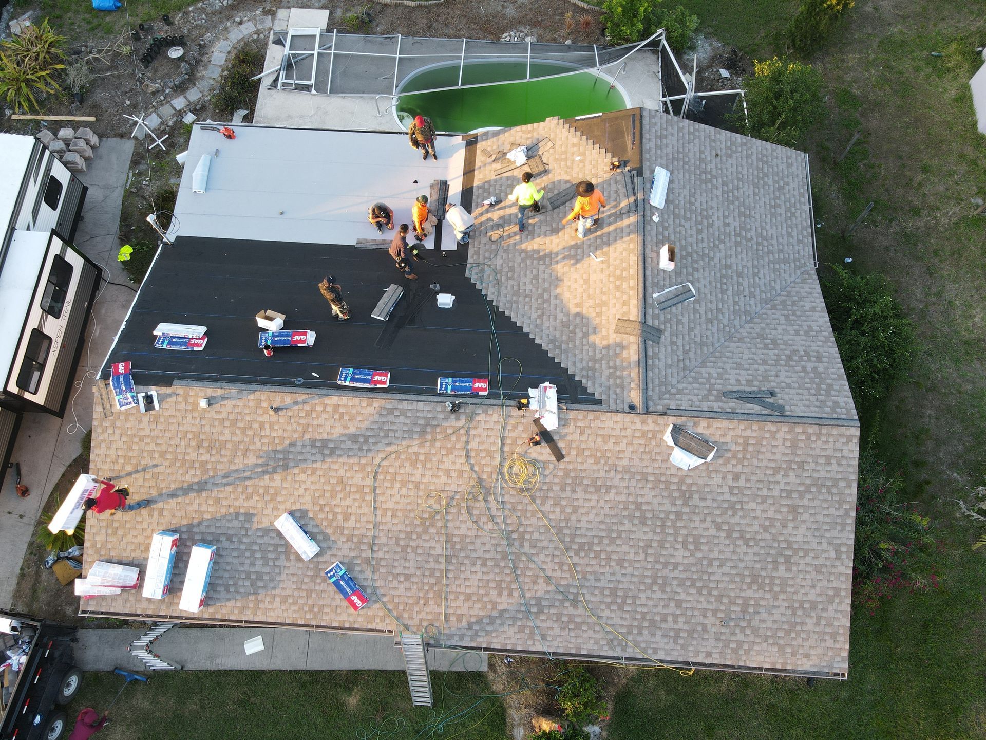 Aerial view of roofers working on a house roof. One side has gray shingles, the other black roofing material.