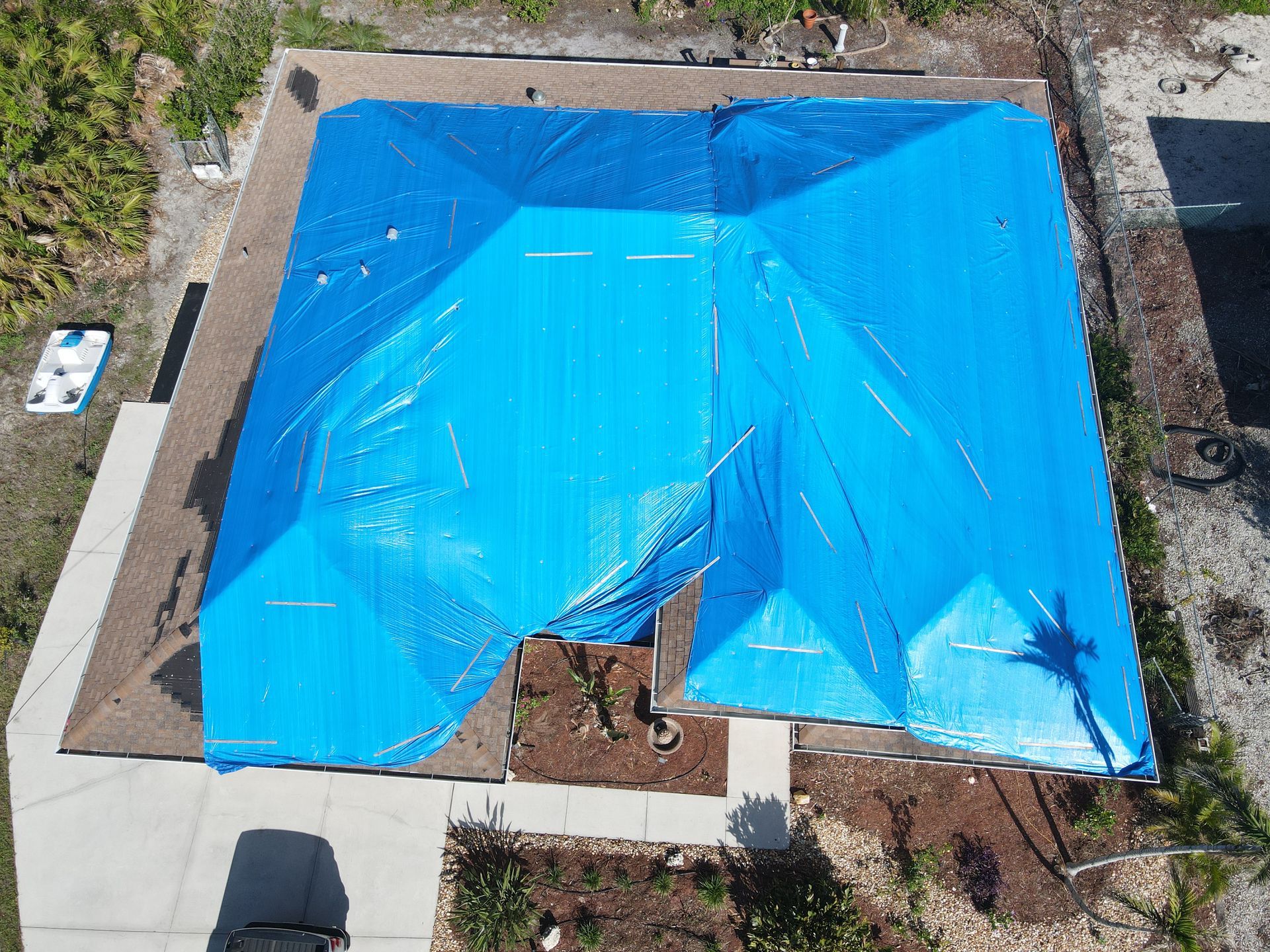 Blue tarp covers a damaged house roof. Aerial view shows the damage.