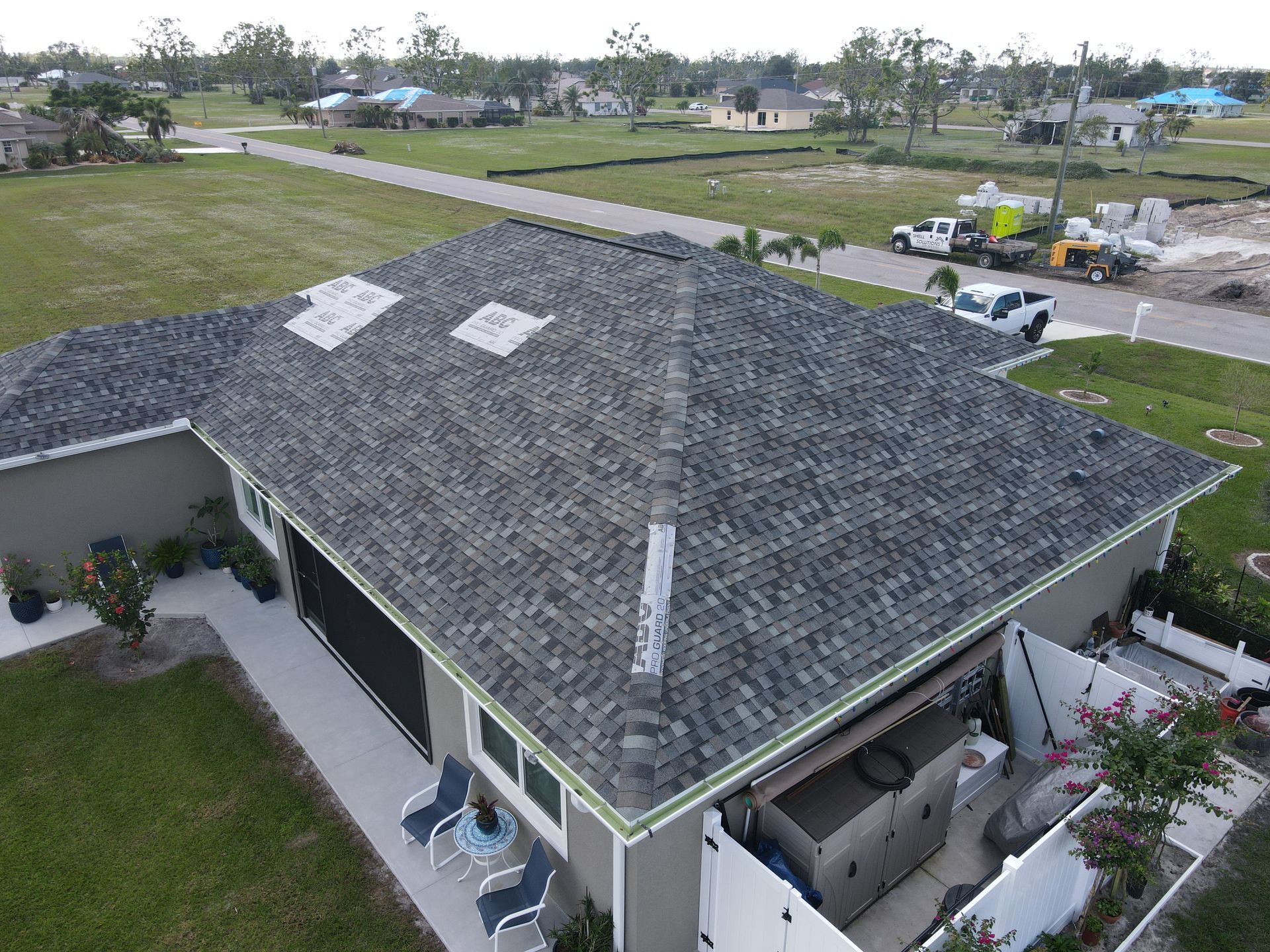 Overhead view of a house with gray roof shingles. White trucks and construction equipment are parked nearby.