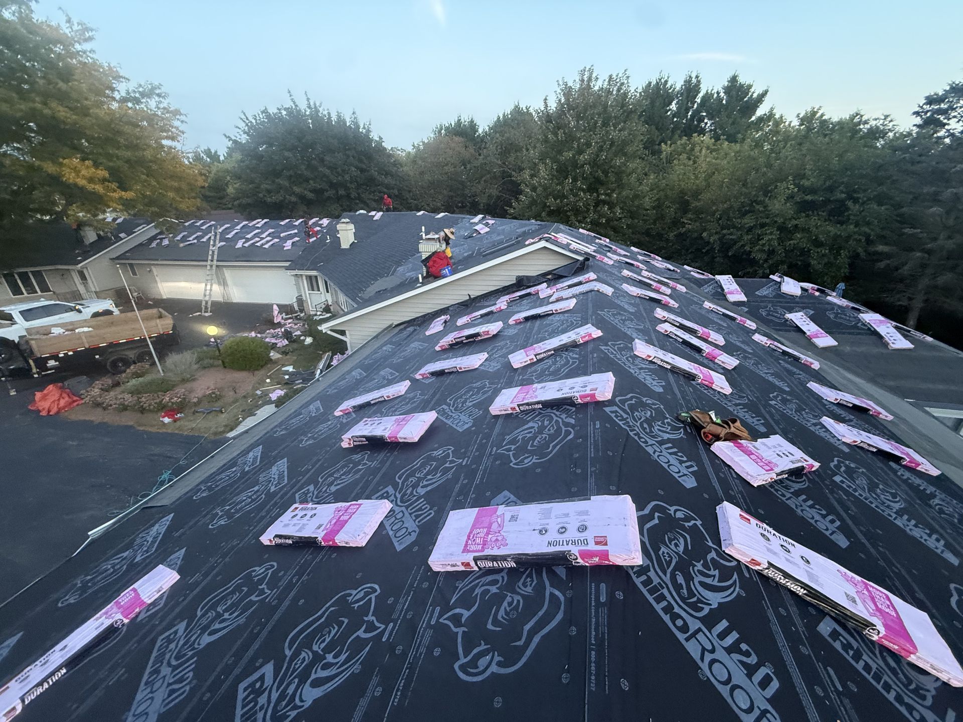 Roofing crew installing shingles on a residential roof, pink insulation visible.
