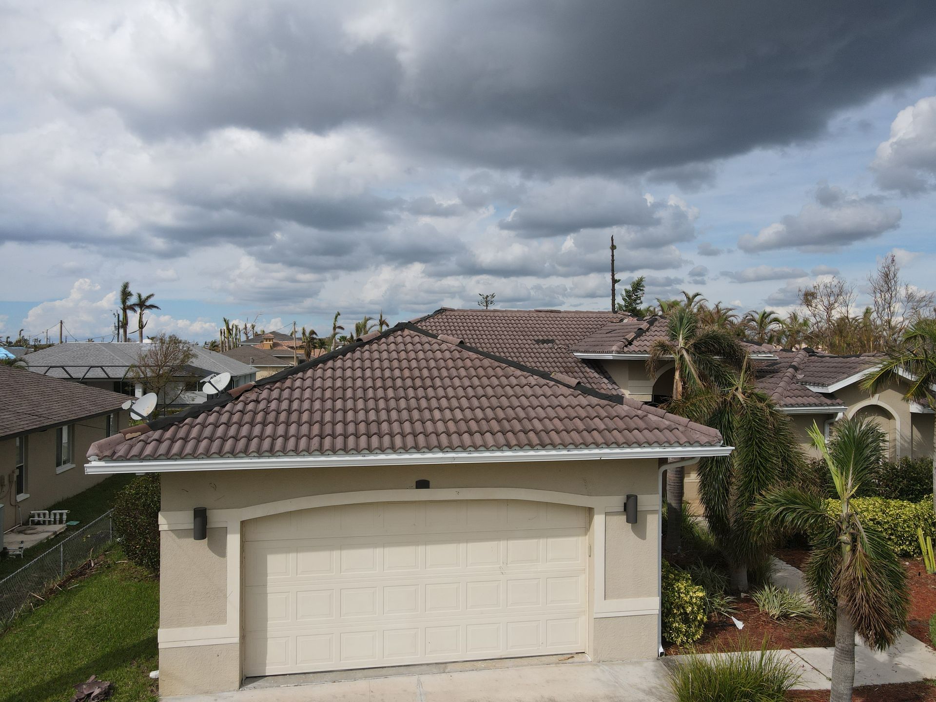 Brown tile roof house with white garage door under cloudy sky.