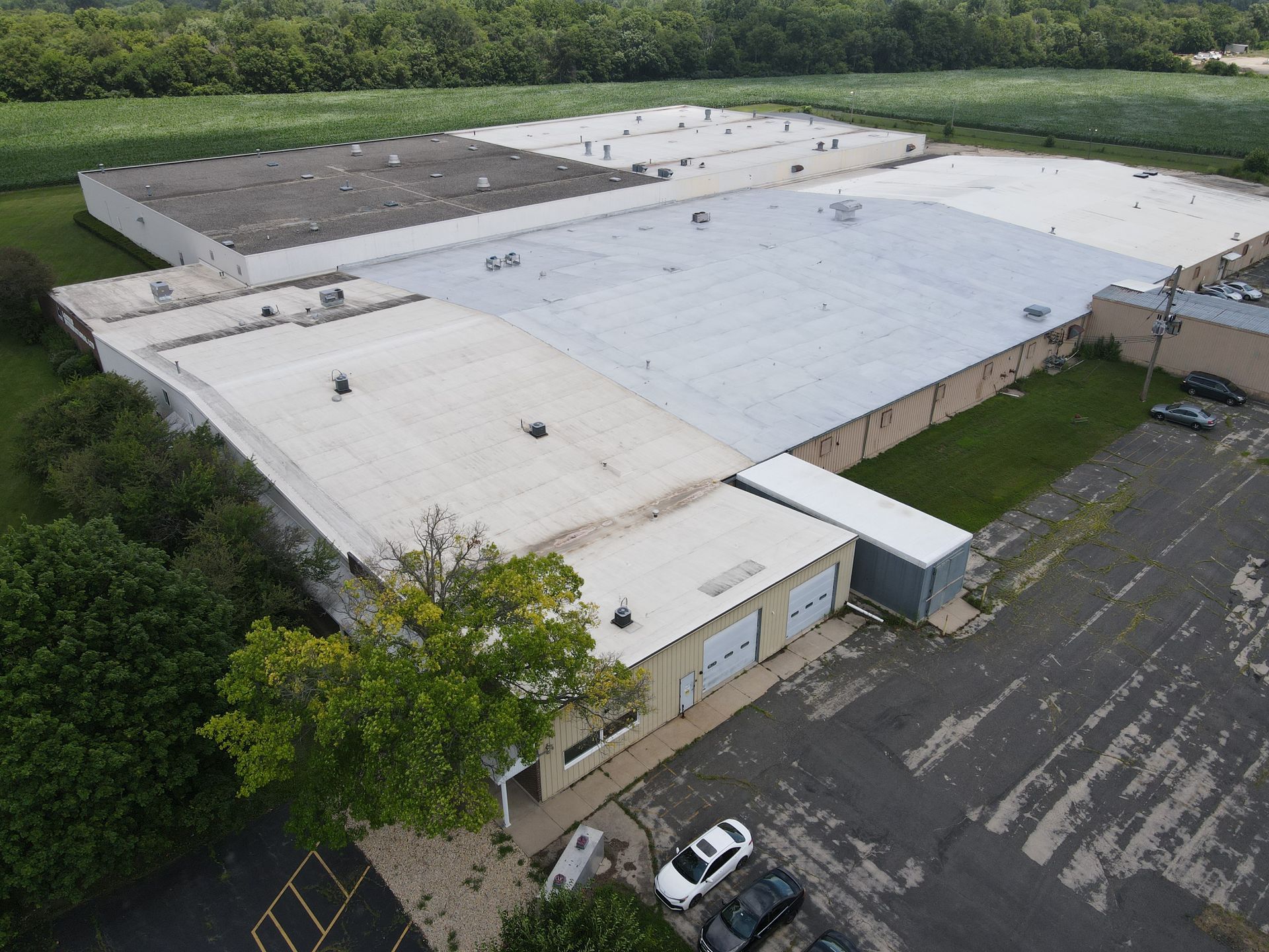 Aerial view of a large industrial building with several sections of flat roofs and parking lot.