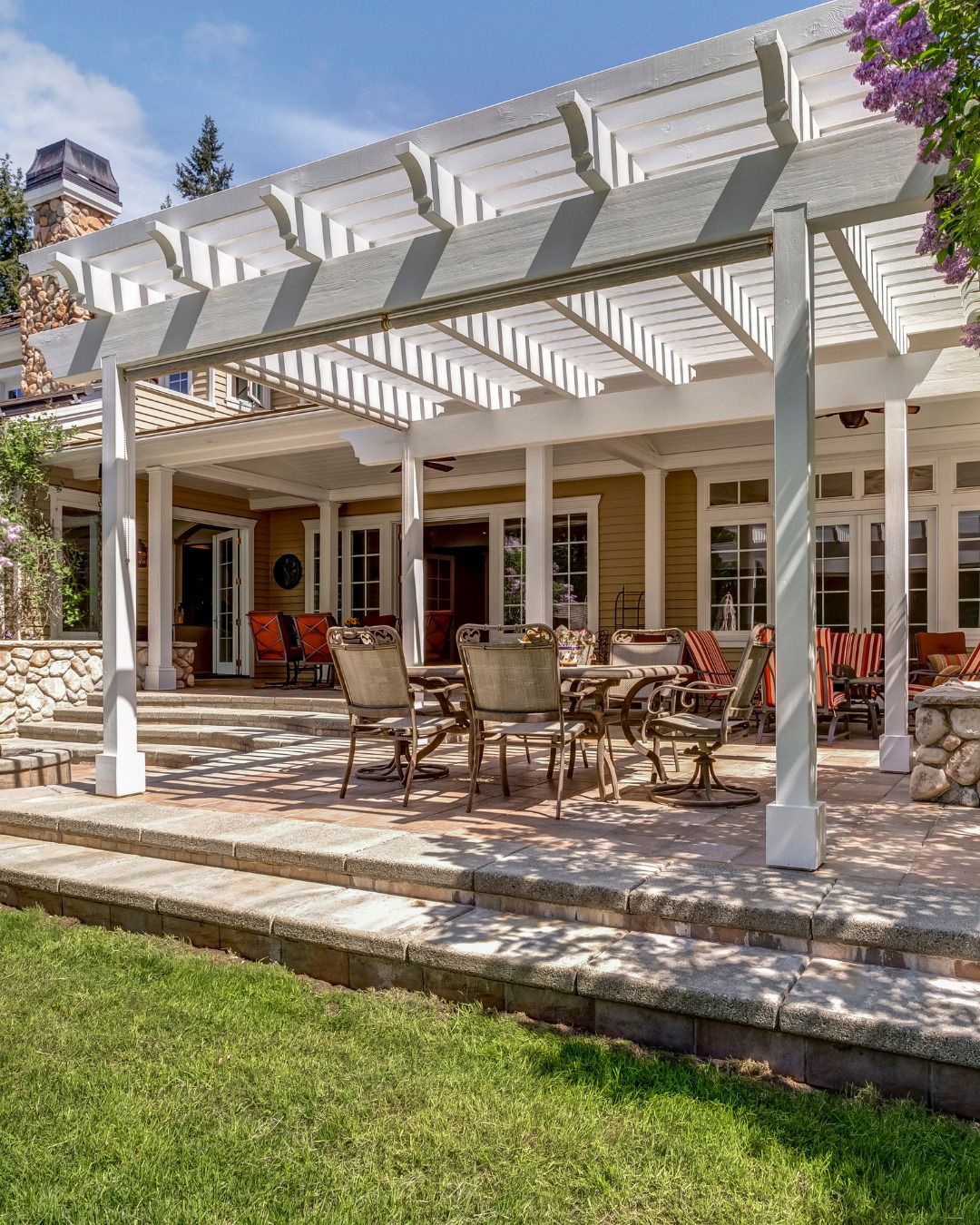 A patio with tables and chairs under a pergola in front of a house.