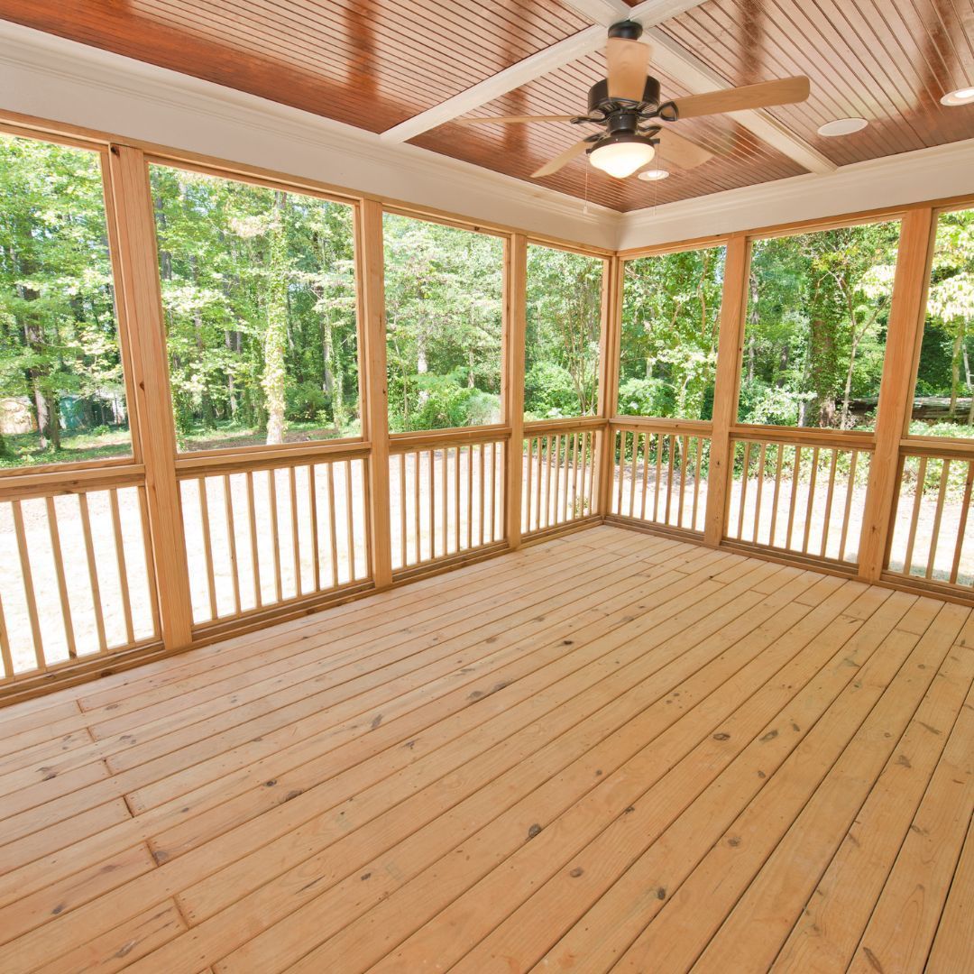An empty screened in porch with a ceiling fan and lots of windows