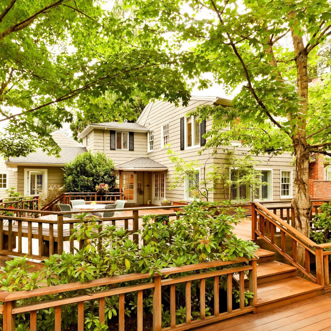 A large house with a wooden deck in front of it surrounded by trees.