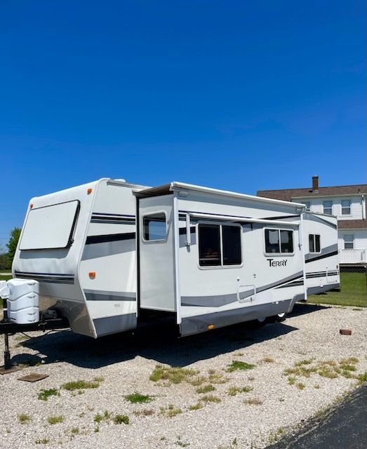 A white rv is parked in a gravel lot in front of a house.