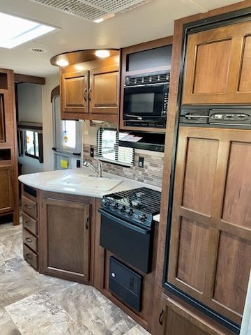 A kitchen in an RV with wooden cabinets, a stove, a sink, and a microwave.