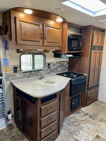 A kitchen in an RV with a sink, stove, microwave, and refrigerator.