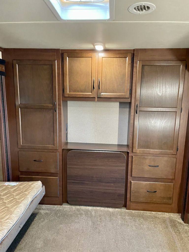 A bedroom with a bed, cabinets, drawers, and a skylight.