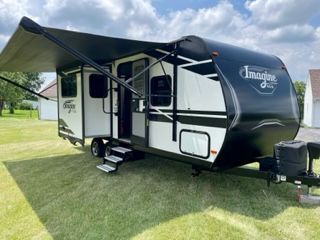 A black and white trailer with an awning is parked in a grassy field.