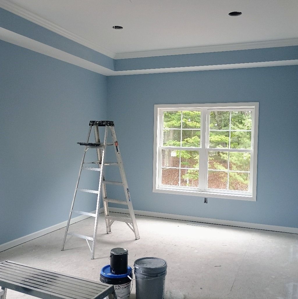 Room with blue walls, white trim, ladder, window, and paint cans.