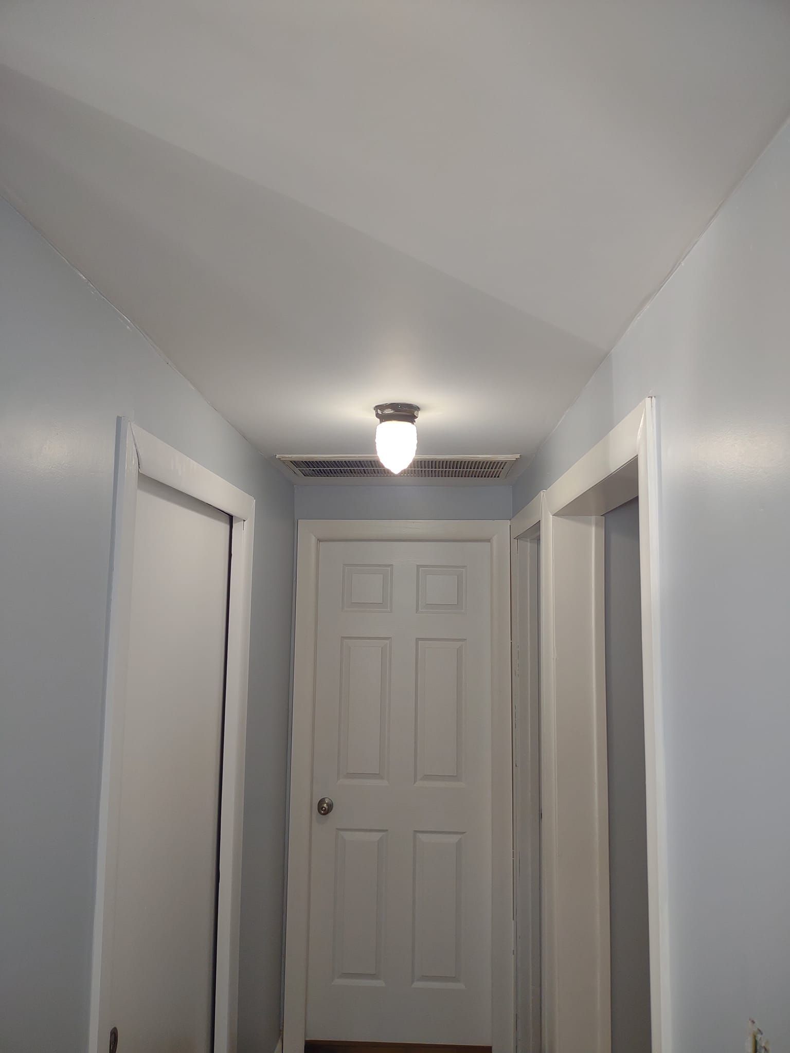 A narrow hallway with a light fixture on the ceiling, doors on either side, and a closed door at the end.